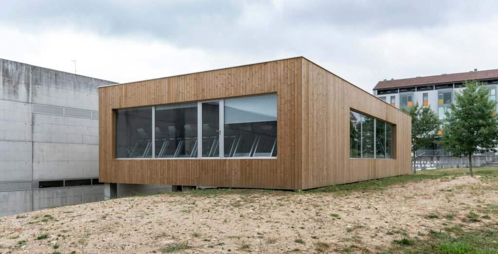 Bâtiment moderne avec un bardage en bois et grandes fenêtres, situé dans un environnement urbain.